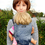 Child carrying a doll in a Didymos toy cotton carrier in the blue and white Kipos design in the frontal position