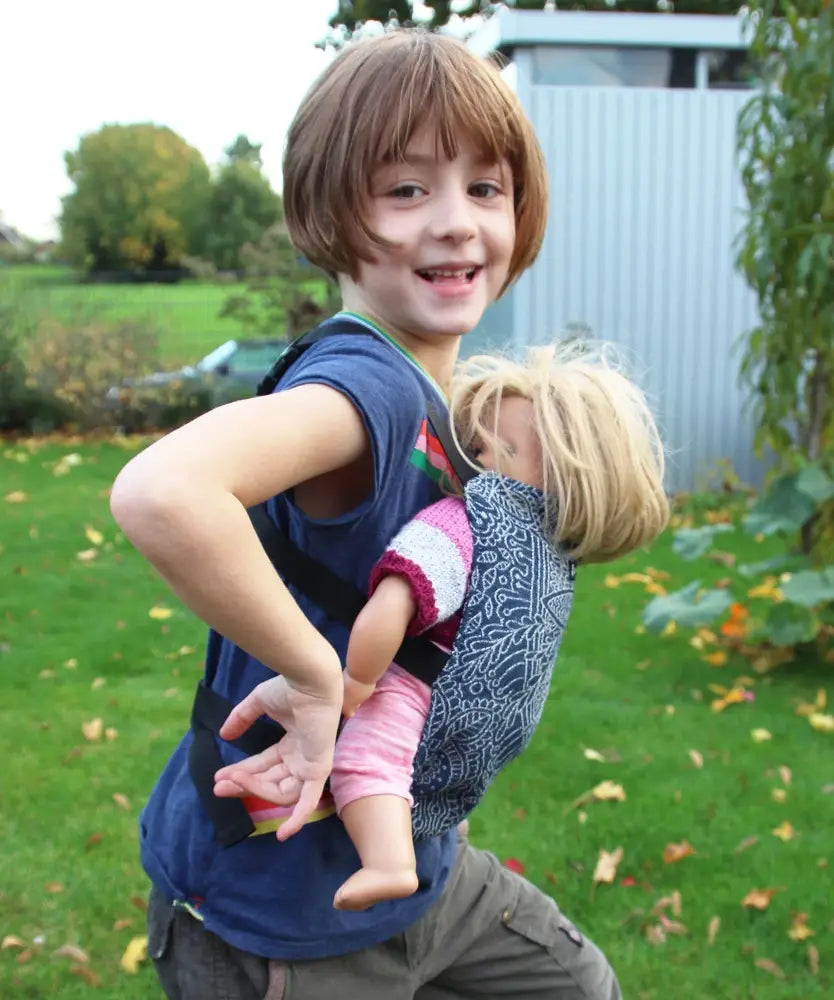 Side of child carrying a doll Didymos toy cotton carrier in the kipost design in the frontal position.