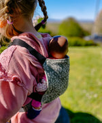 Back of child carrying a doll in a Didymos toy carrier in olive twig