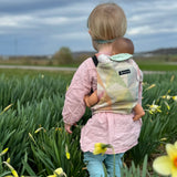 Child carrying a doll in a Didymos toy carrier in the zephyr design in a grassy field