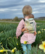 Child carrying a doll in a Didymos toy carrier in the zephyr design in a grassy field