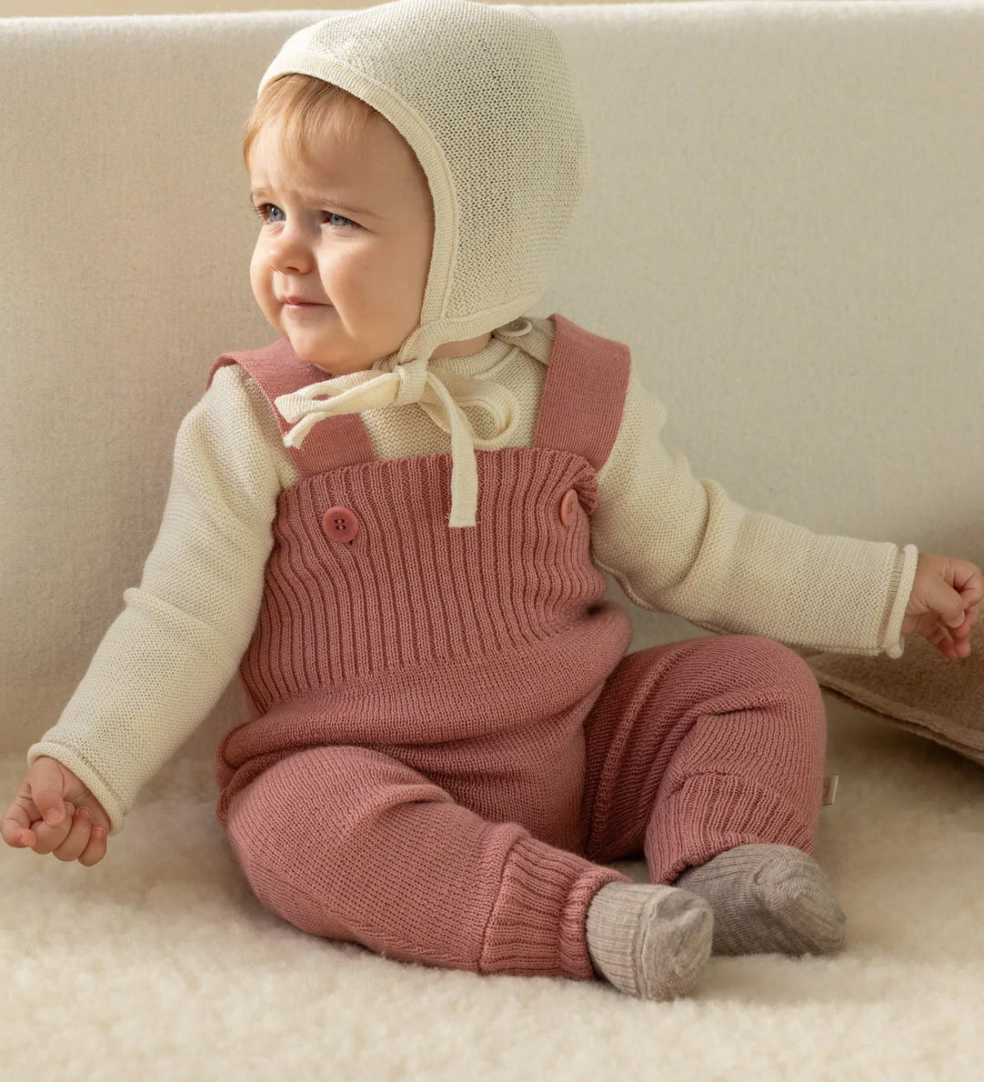 A baby dressed in a full organic merino wool outfit by Disana, including the knitted dungarees and natural Melange jumper