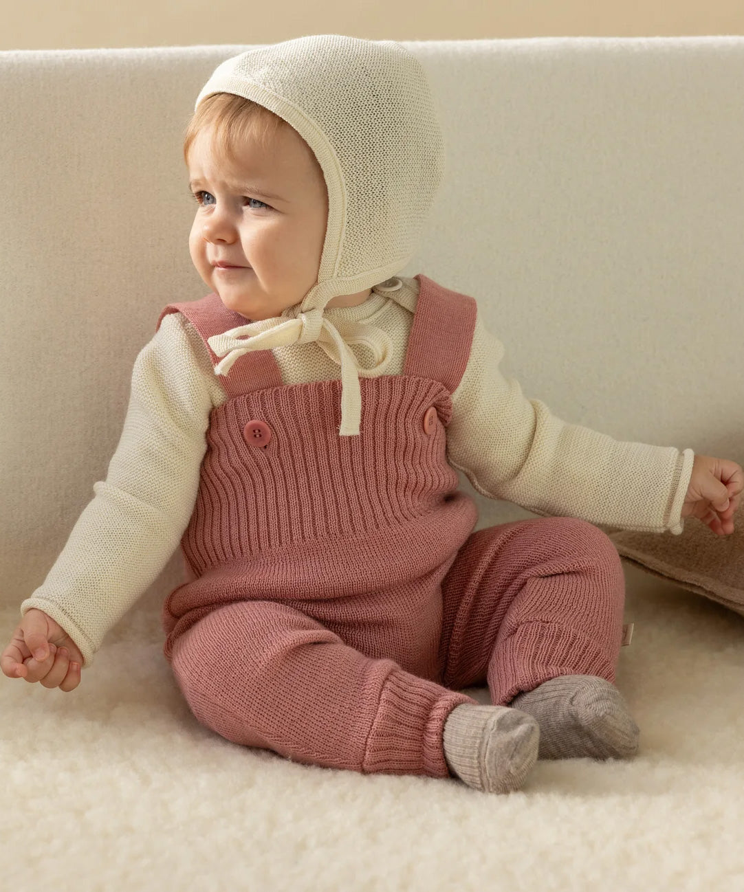 A baby dressed in a full organic merino wool outfit by Disana, including the knitted dungarees and natural Melange jumper
