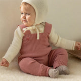 A baby dressed in a full organic merino wool outfit by Disana, including the knitted dungarees and natural Melange jumper