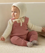 A baby dressed in a full organic merino wool outfit by Disana, including the knitted dungarees and natural Melange jumper