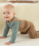 Baby crawling indoors wearing caramel brown Disana knitted merino wool dungarees over a long-sleeved top.