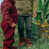 Toddler wearing deep maroon knitted merino wool dungarees and matching wool layers by Disana, standing in grass outdoors.