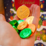 Close up of a hand holding the fairtrade Divine dark chocolate coins in front of a Divine christmas calendar