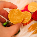 Close up of a hand holding a Divine ethical milk chocolate coin over a fluffy blanket