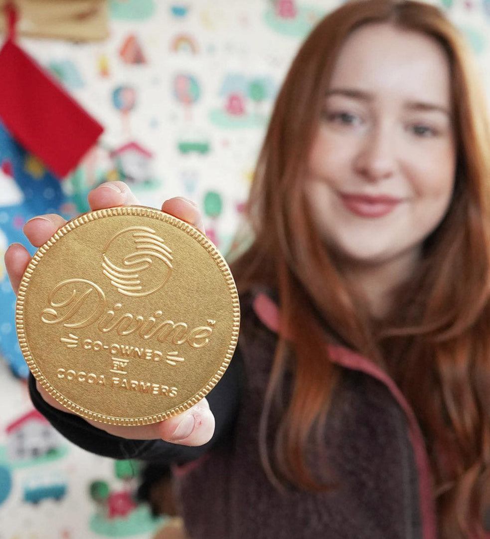 Close up of woman holding up the Divine giant Fairtrade milk chocolate coin in front of a white patterned wall