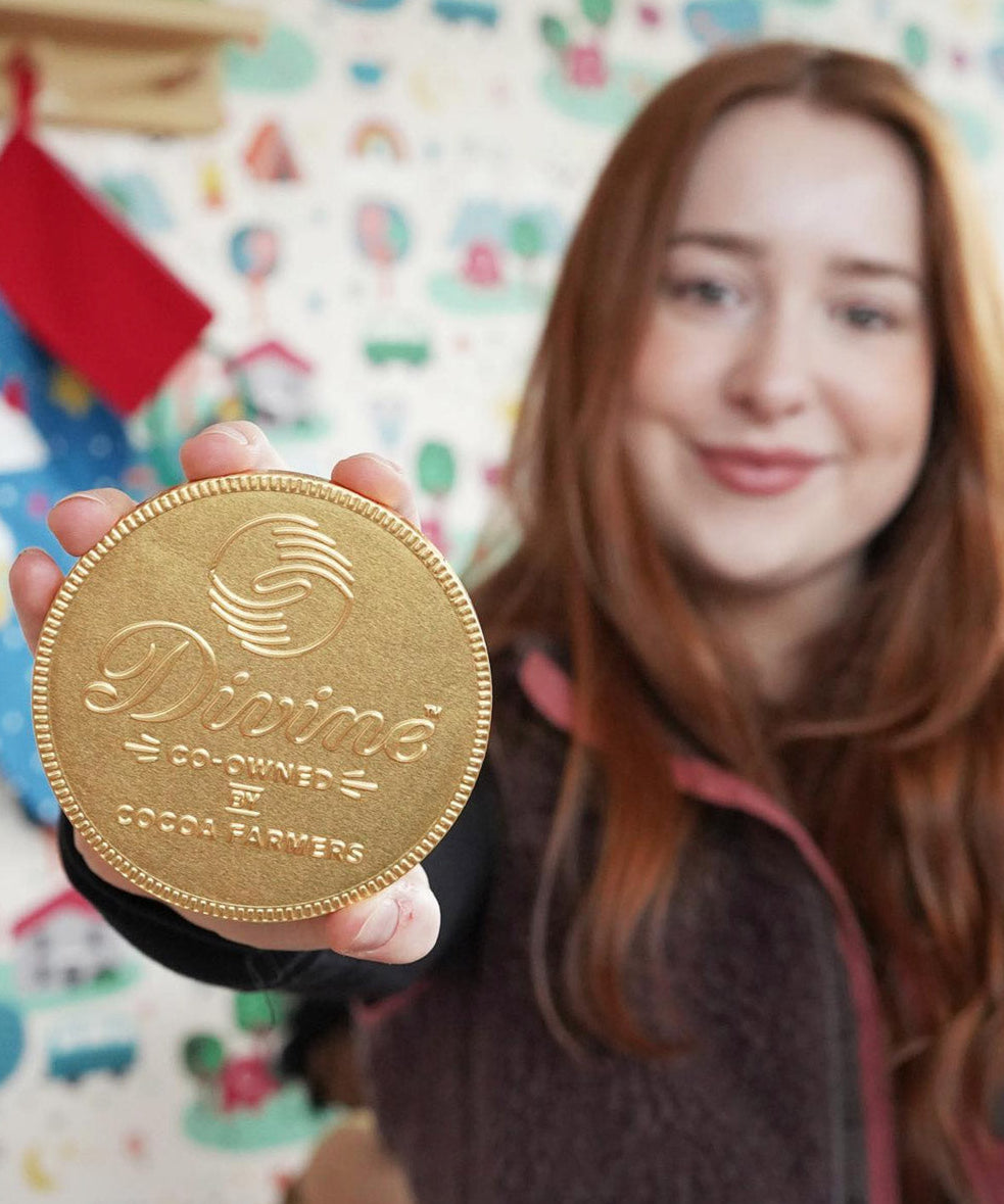 Close up of woman holding up the Divine giant Fairtrade milk chocolate coin in front of a white patterned wall