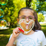 Child blowing a bubble through a hear shaped bubble Hand Wand with trees in the background