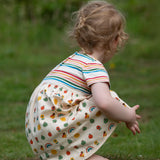 Crouching child wearing the Little Green Radicals Easy Peasy organic cotton dress with a cream rainbow striped body and nature patterned skirt.