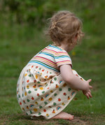 Crouching child wearing the Little Green Radicals Easy Peasy organic cotton dress with a cream rainbow striped body and nature patterned skirt.