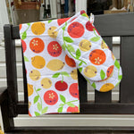 DUNS eco-friendly organic cotton oven glove and tea towel in the citrus print hanging over the end of a black bench