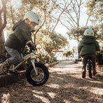 2 children sat on Early Rider aluminium balance bikes on a rock in front of the sea