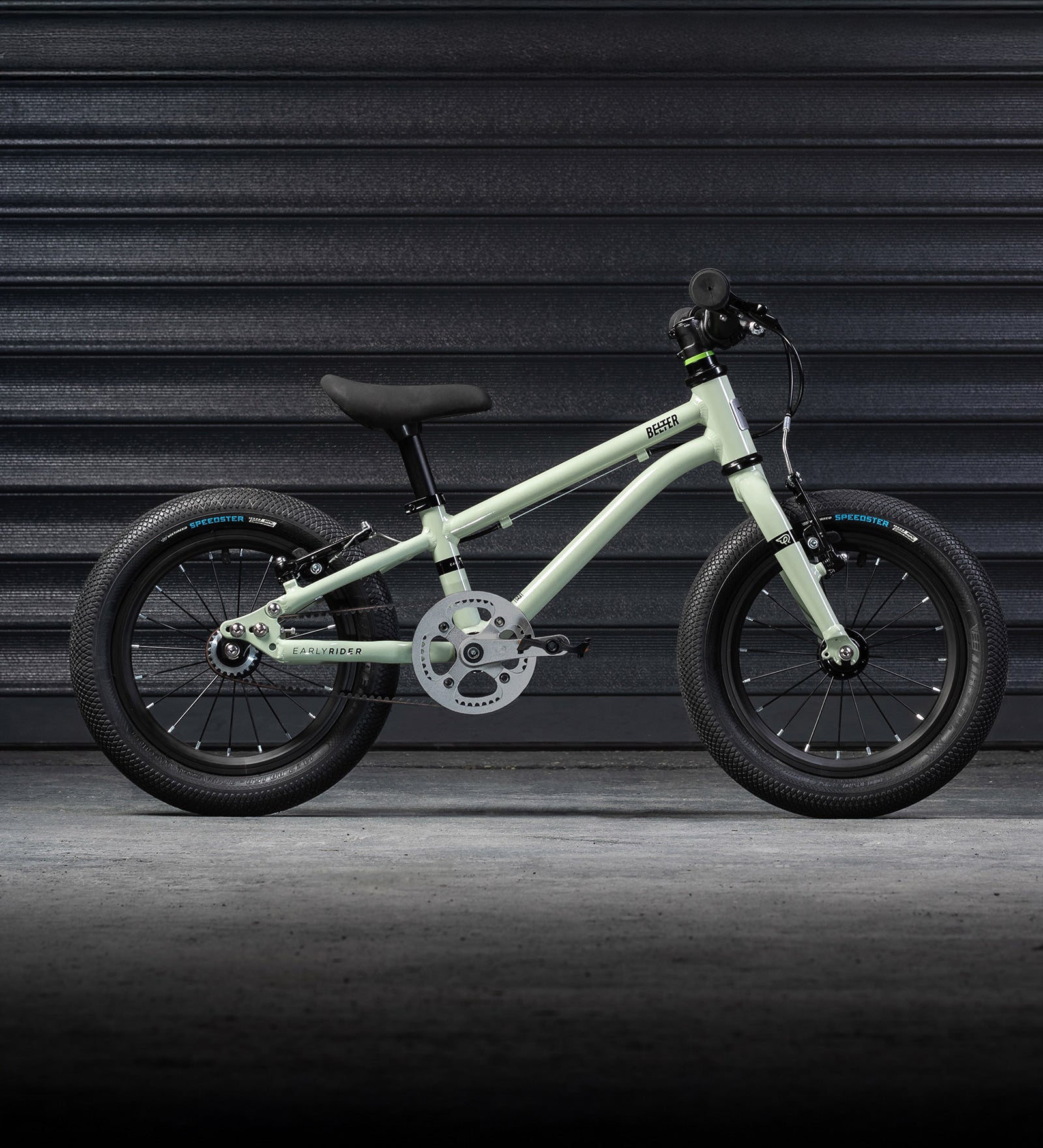 The Early Rider Belter 14" Kids Pedal Bike for 3-5 Years in sage green. The bike is shown in front of black garage doors. Babipur are official stockists of Early Rider. 