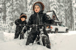 2 kids sat on some Early Rider 12 inch balance bikes in some deep snow