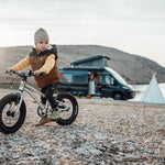 Girl sat on an Early Rider 14 inch seeker bicycle in front of a black campervan