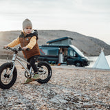 Girl sat on an Early Rider 14 inch seeker bicycle in front of a black campervan