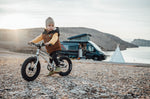 Girl sat on an Early Rider 14 inch seeker bicycle in front of a black campervan