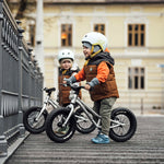 2 children sat on Early Rider big foot balance bikes next to a metal fence