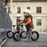 2 children sat on Early Rider big foot balance bikes next to a metal fence