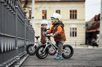 2 children sat on Early Rider big foot balance bikes next to a metal fence