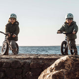 2 children sat on Early Rider aluminium balance bikes on a rock in front of the sea