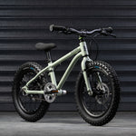 A sage green coloured Early Rider X16 children's bike placed in front of black garage doors.