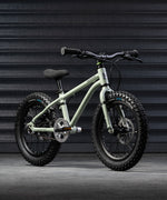 A sage green coloured Early Rider X16 children's bike placed in front of black garage doors.