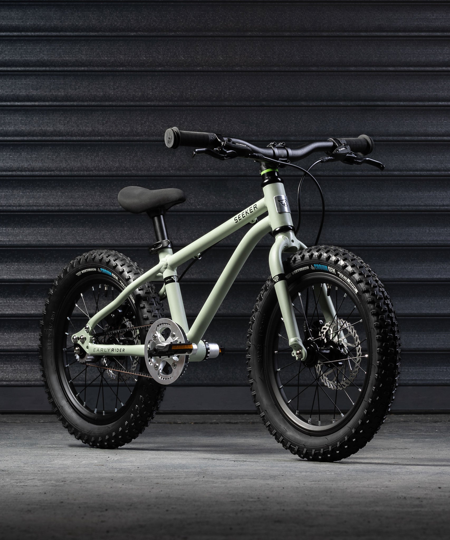 A sage green coloured Early Rider X16 children's bike placed in front of black garage doors.