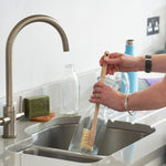 Person using a Ecoliving Wooden Bottle Brushto wash a glass carafe in a kitchen sink
