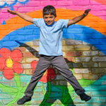 A school boy making a star jump in the air, wearing the Eco Outfitters organic and fair trade cotton polo shirt and school trousers.