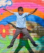 A school boy making a star jump in the air, wearing the Eco Outfitters organic and fair trade cotton polo shirt and school trousers.