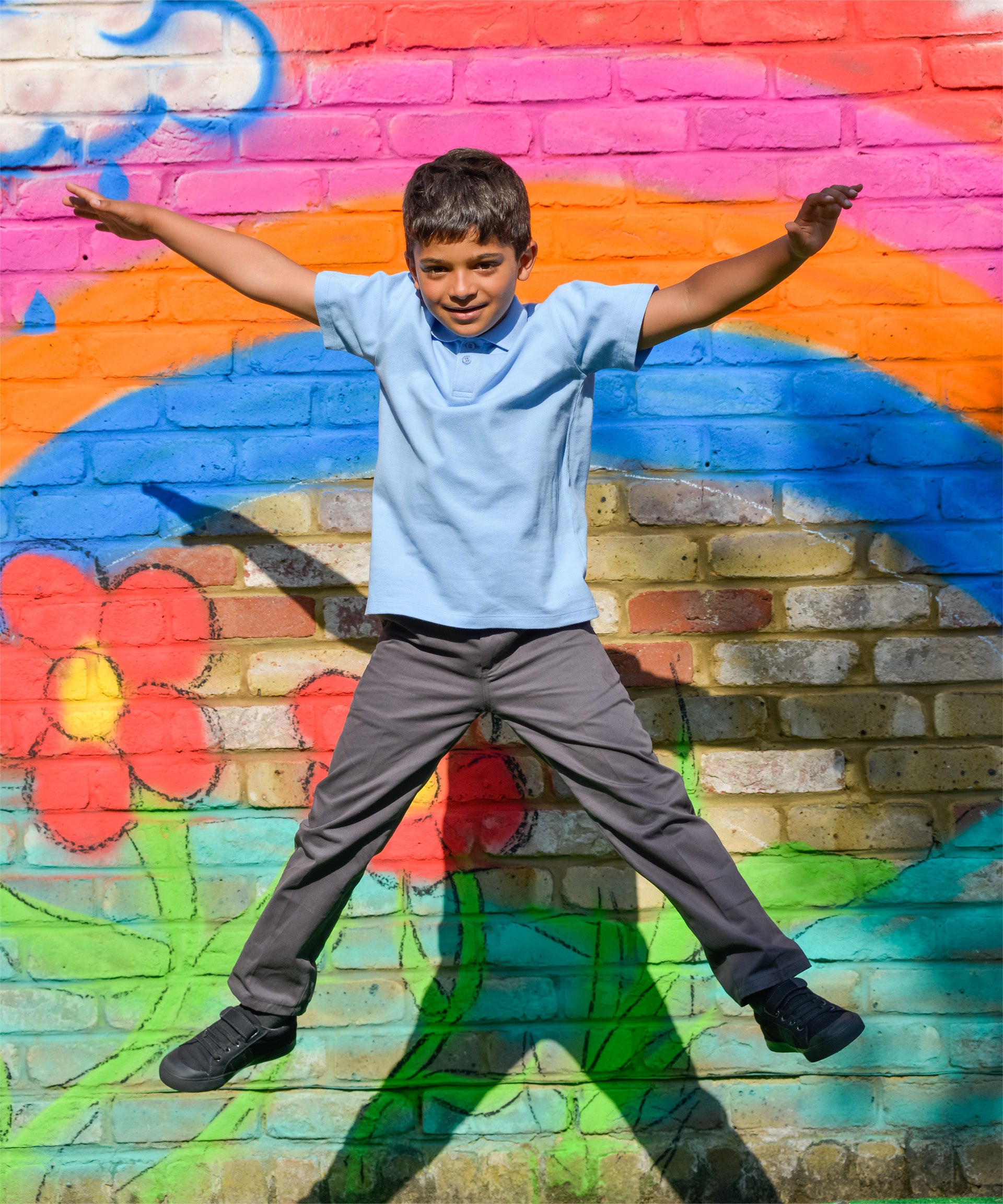 A school boy making a star jump in the air, wearing the Eco Outfitters organic and fair trade cotton polo shirt and school trousers.
