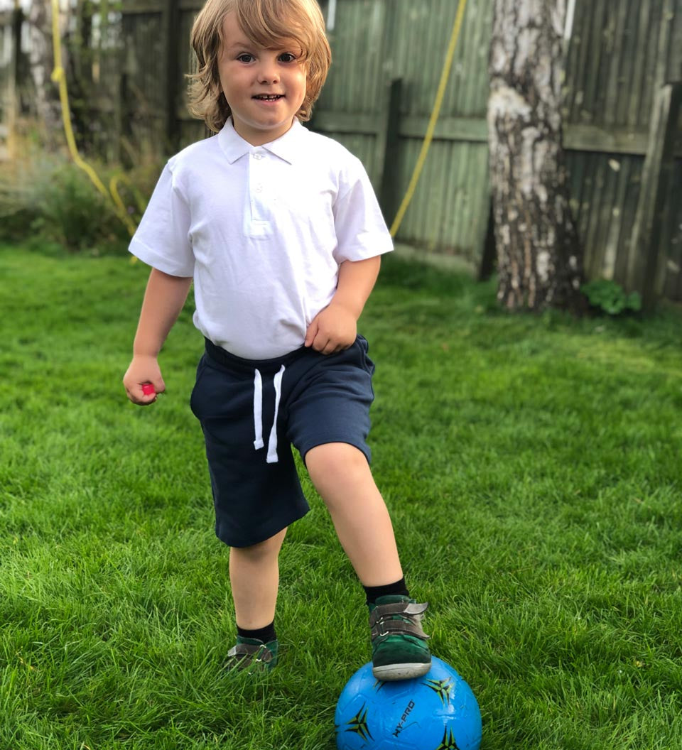 A child wearing the white Eco Outfitters organic school polo shirt and shorts, whilst playing football in the garden.
