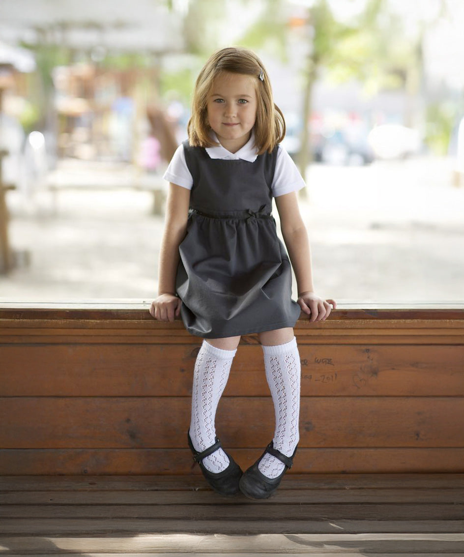 A little girl wearing the Eco Outfitters organic and fair trade cotton school pinafore dress in grey with a bow detail.