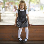 A little girl wearing the Eco Outfitters organic and fair trade cotton school pinafore dress in grey with a bow detail.
