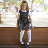 A little girl wearing the Eco Outfitters organic and fair trade cotton school pinafore dress in grey with a bow detail.