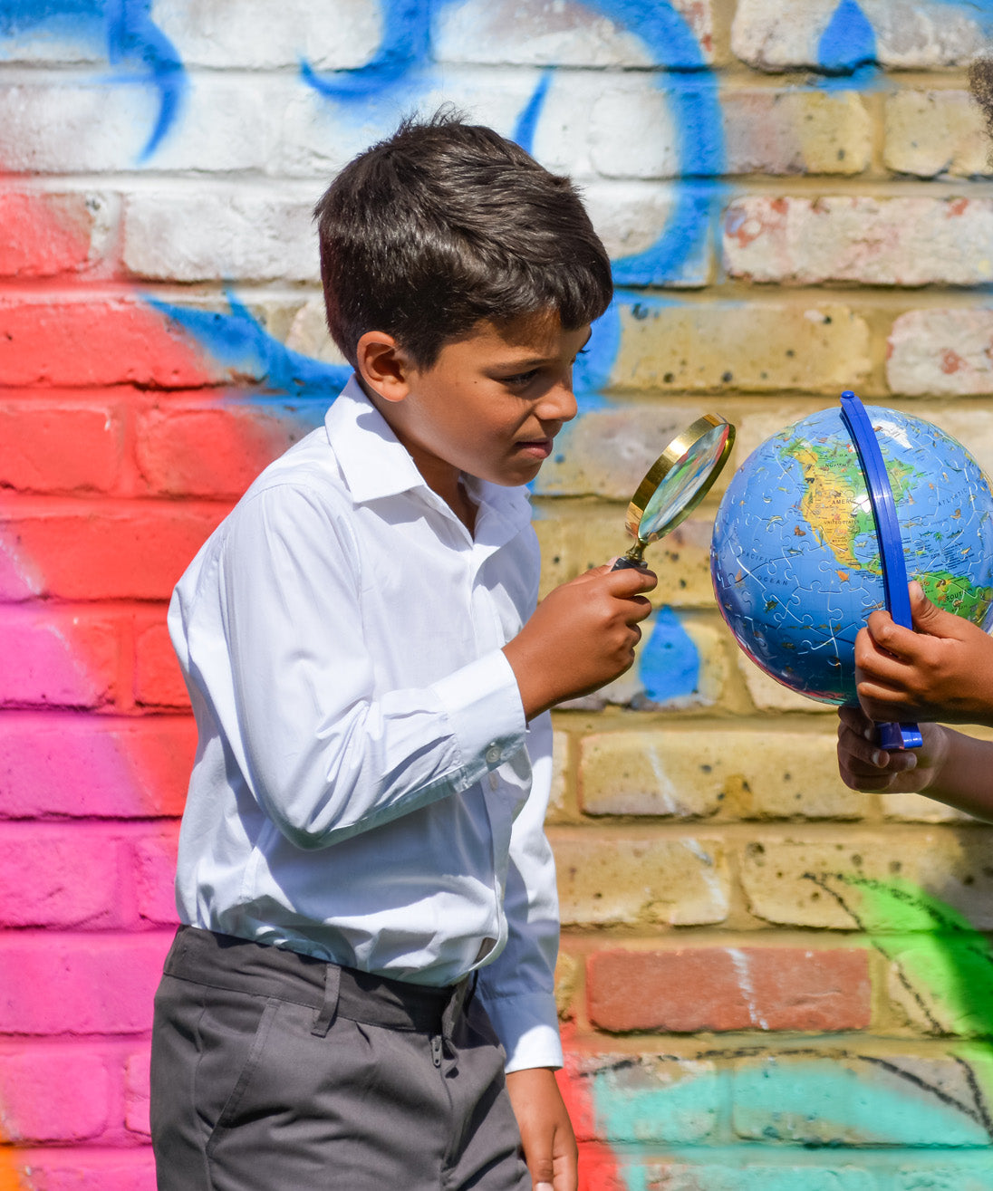 A boy wearing The Eco Outfitters Fair Trade and organic cotton school uniform shirt, and holding a magnifying glass