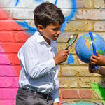 A boy wearing The Eco Outfitters Fair Trade and organic cotton school uniform shirt, and holding a magnifying glass