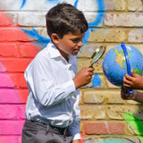 A boy wearing The Eco Outfitters Fair Trade and organic cotton school uniform shirt, and holding a magnifying glass