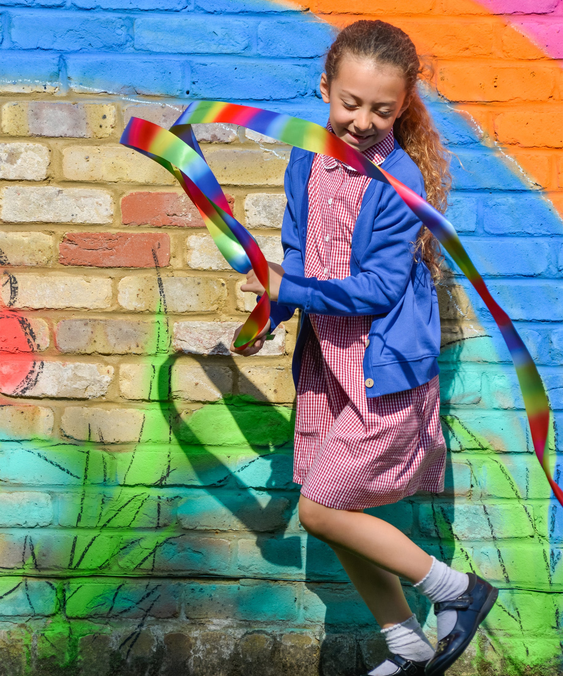 A little girl playing in the schoolyard, wearing the Eco Outfitters organic and fair trade cotton gingham summer dress and school cardigan in blue.