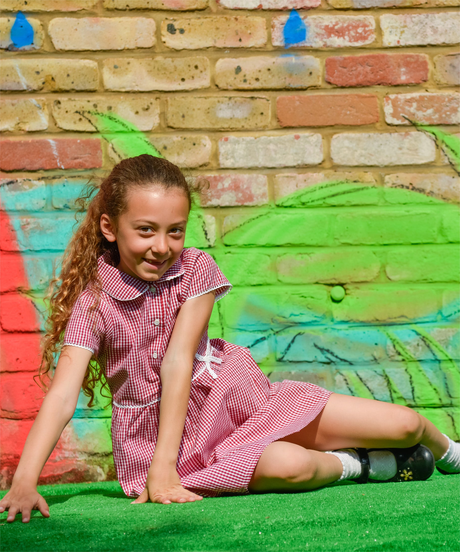 A little girl wearing The Eco Outfitters organic and fair trade cotton school summer dress in red gingham.
