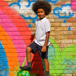 A child wearing the white Eco Outfitters organic school polo shirt and shorts, whilst playing football in the garden.