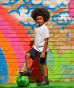 A child wearing the white Eco Outfitters organic school polo shirt and shorts, whilst playing football in the garden.