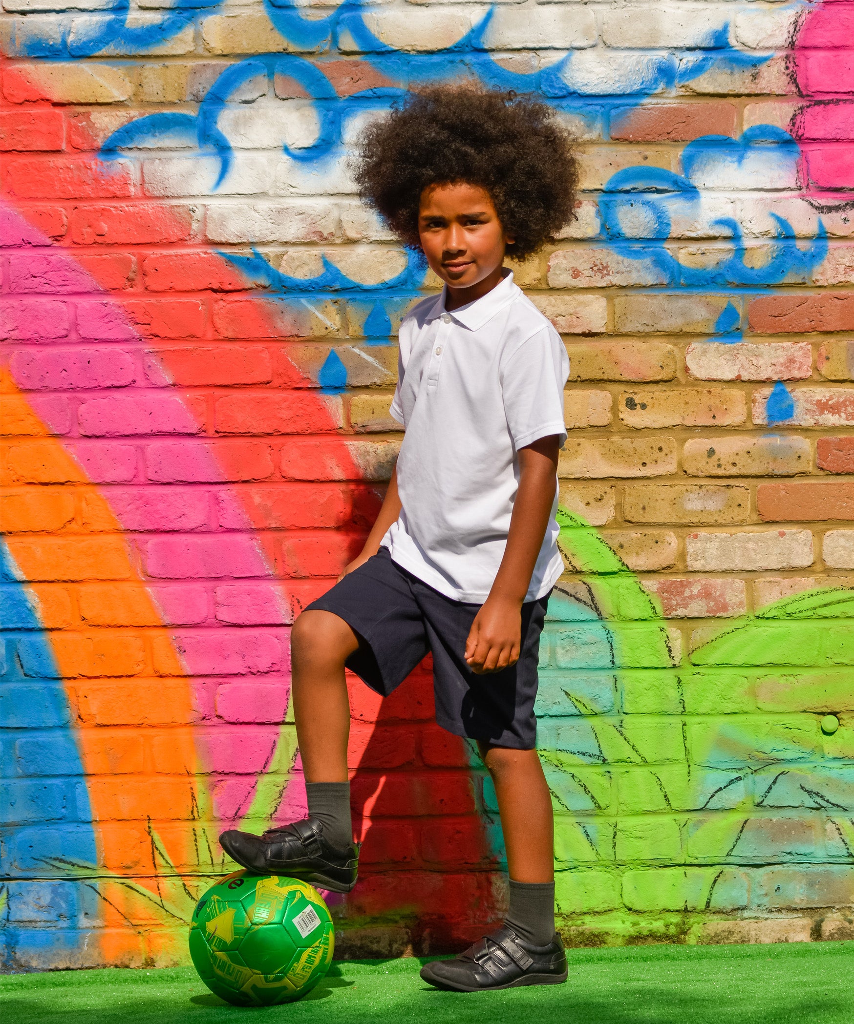A child wearing the white Eco Outfitters organic school polo shirt and shorts, whilst playing football in the garden.