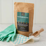 Ecoliving Bicarbonate Of Soda pictured next to green rubber gloves and a wooden scoop placed in a glass tub