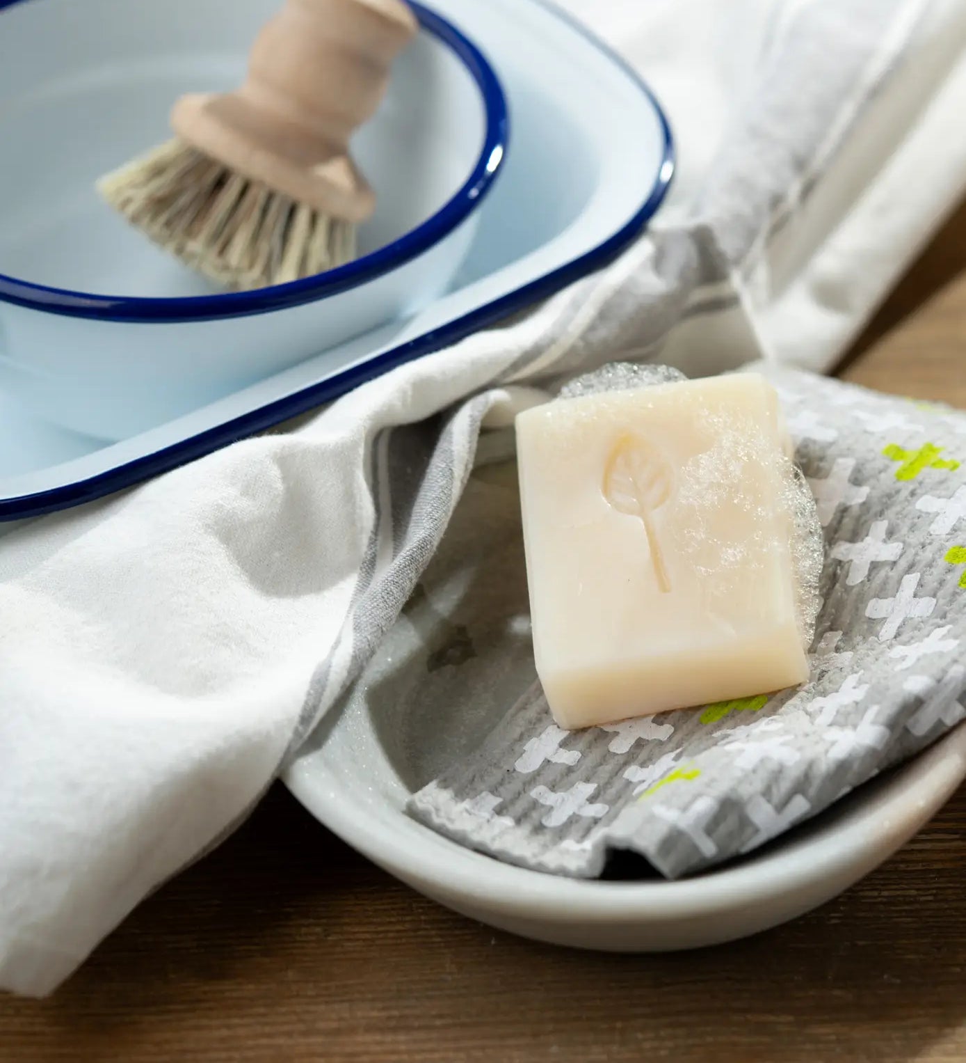 Lathered blossom breeze Ecoliving 100% vegan dish soap bar in a small bowl with a kitchen items in the background.